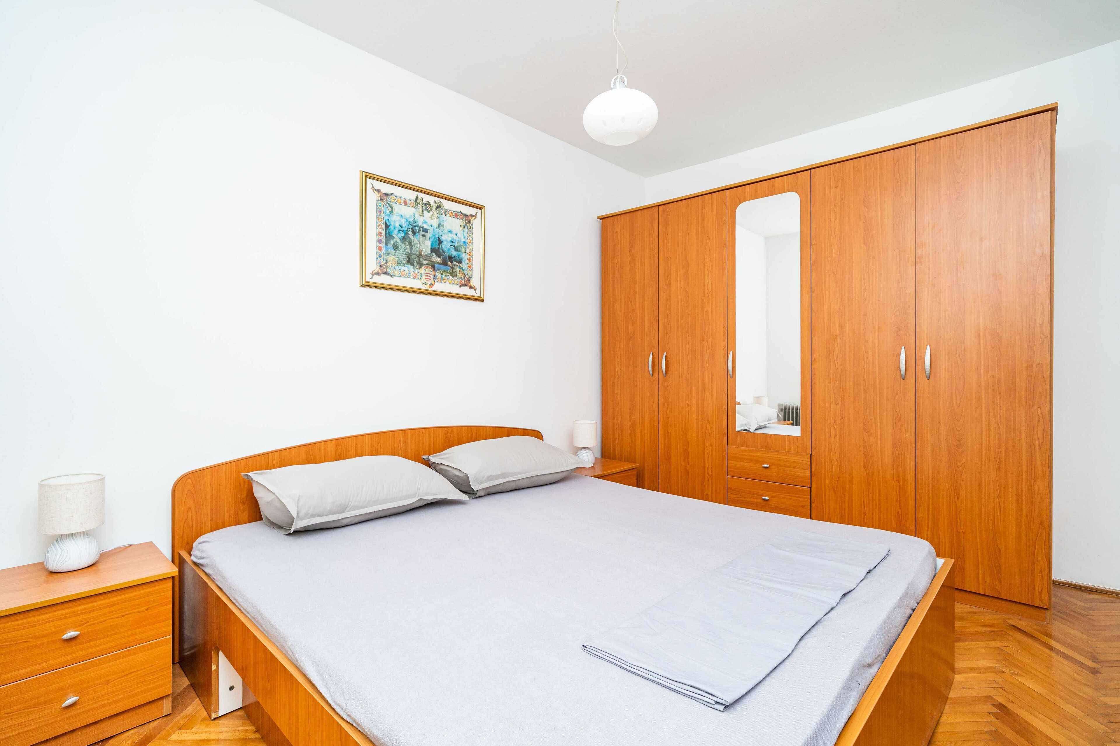 Quarto com cama de madeira, mesa de cabeceira, guarda-roupa e um quadro emoldurado na parede.