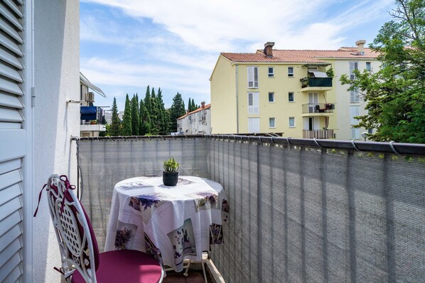 Un balcon avec une table et une chaise, un pot de fleurs et une vue sur les bâtiments environnants.
