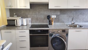 A modern kitchen with white cabinets, a built-in microwave, toaster, and dishwasher. There's a sink with a faucet and a washing machine. - NIGRAN, Studio 10 minutes from Playa America (NIGRAN)