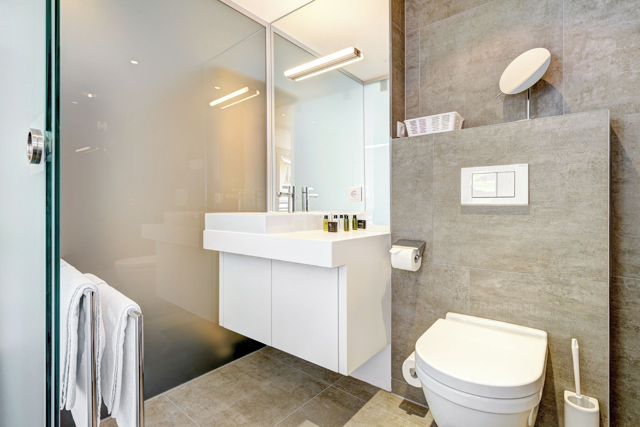 A modern bathroom with a glass shower enclosure, a white sink, and a toilet.