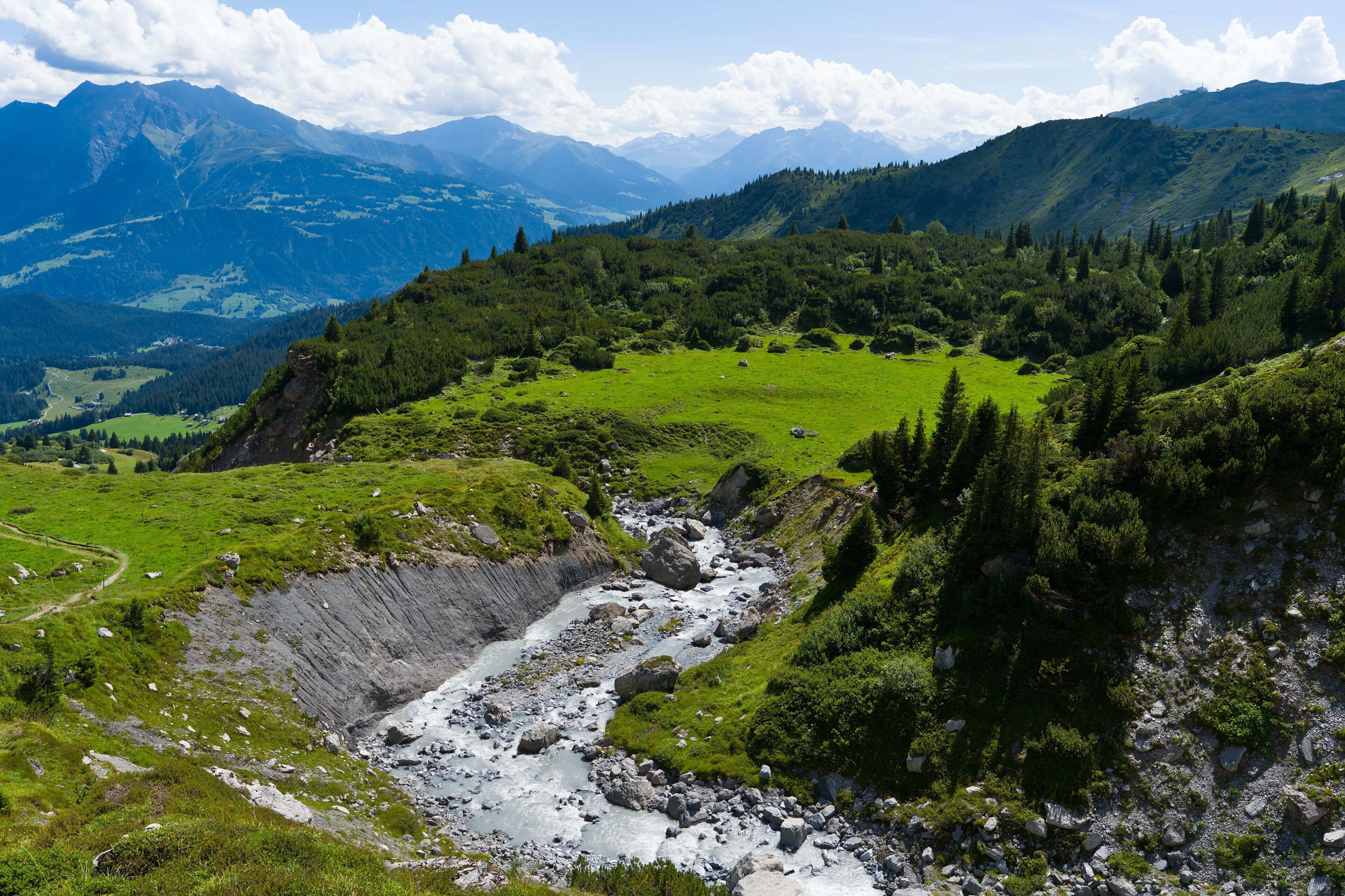 A mountainous landscape with a river, green fields, and distant mountains.