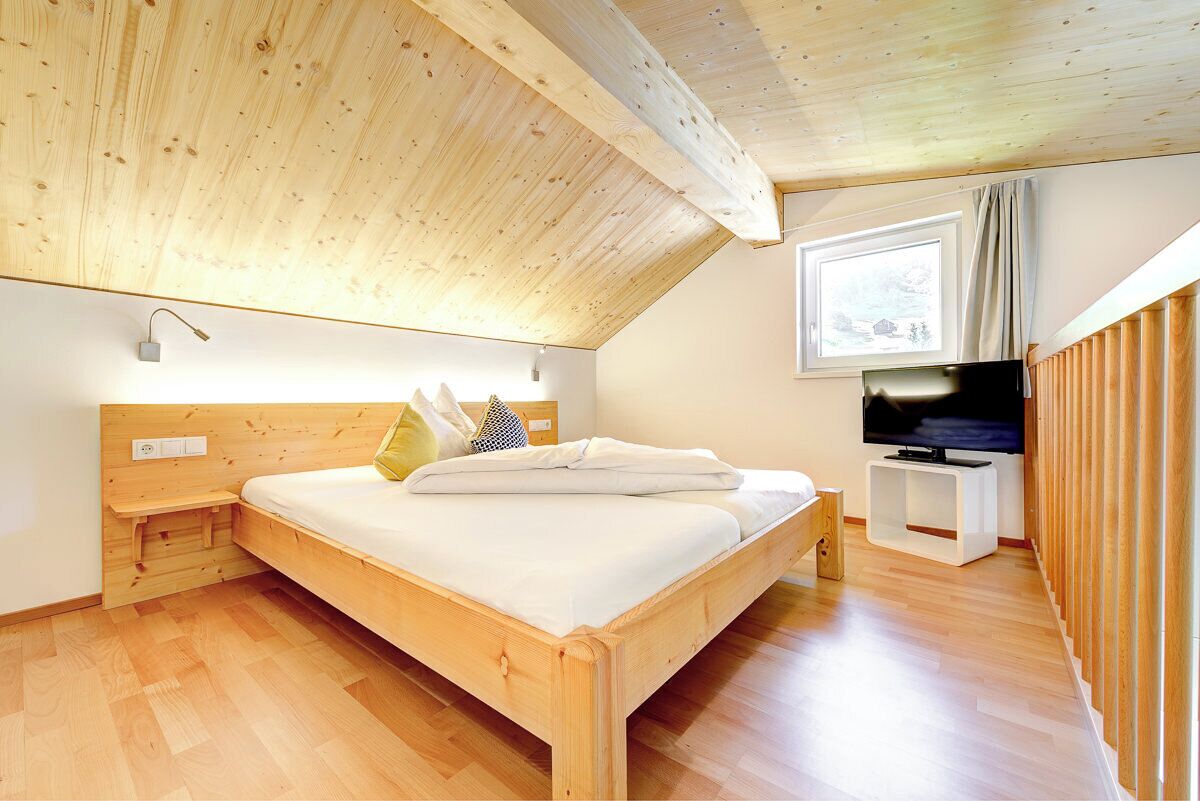 A bedroom with a wooden ceiling, a bed, a TV stand, and a window.