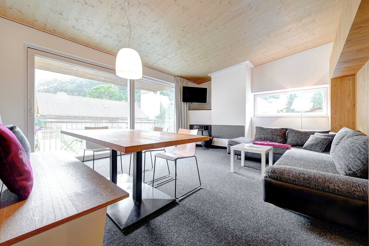 Ein modernes Wohnzimmer mit Holzboden, einem Esstisch, einer Couch und einem an der Wand befestigten Fernseher.
