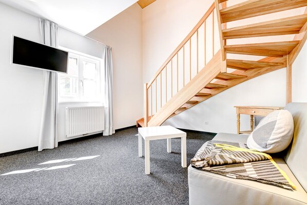 A modern living room with a staircase, a flat-screen TV, a white table, and a sofa with a throw blanket. - Hotel Lün (Brand)