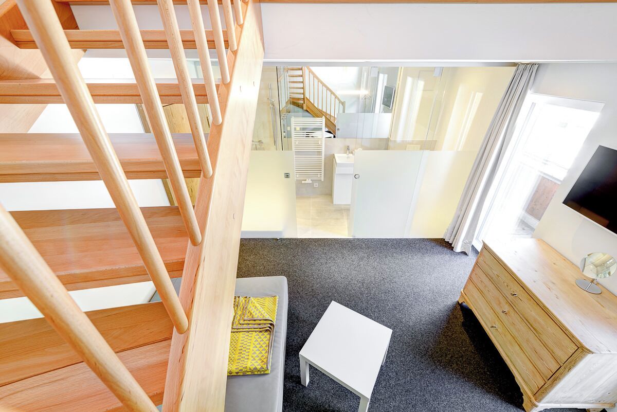 A modern interior with a staircase, a small table, a sofa, a wooden dresser, and a TV.