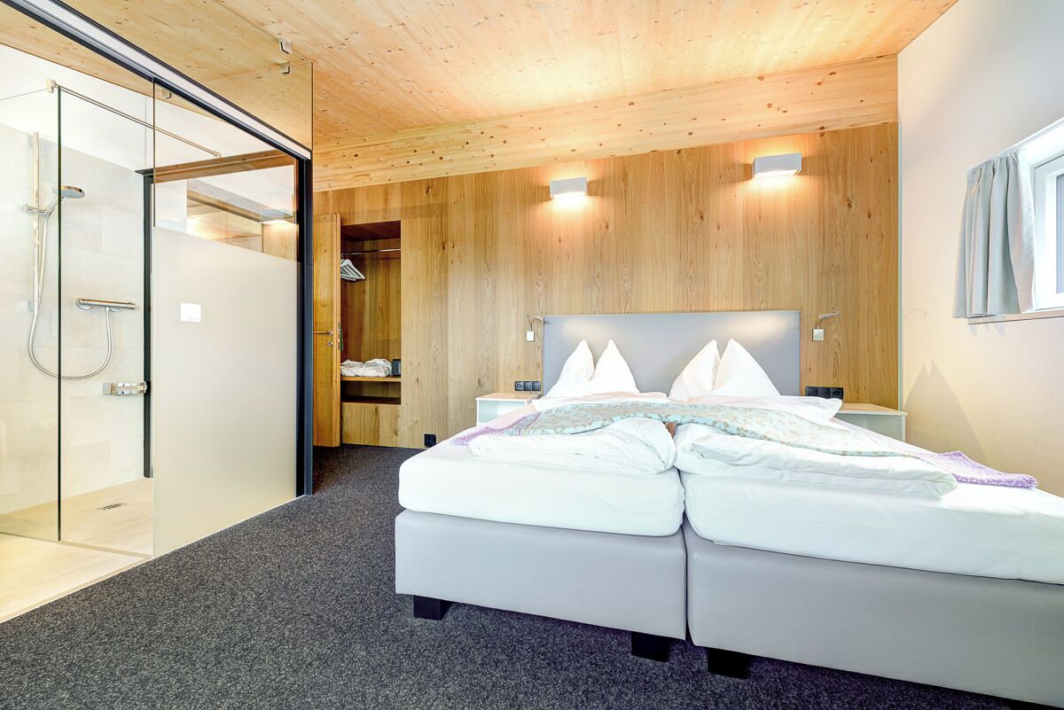 Une chambre moderne avec un plafond en bois, un grand lit avec une literie blanche, une douche en verre et une armoire en bois.