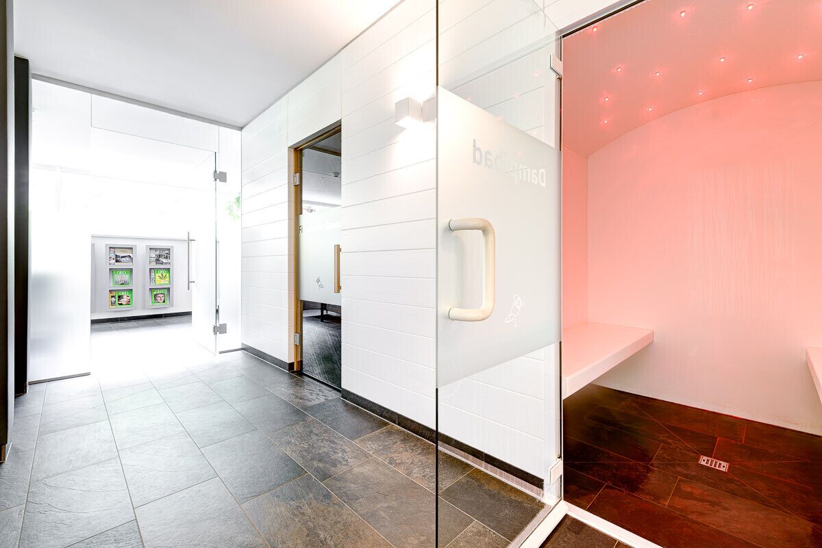 A modern hotel lobby with a glass partition, a reception desk, and a wall-mounted information board.