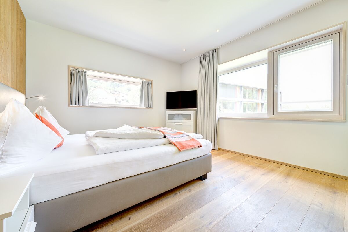 A modern bedroom with a large bed, a flat-screen TV, and a window with curtains.