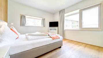 A modern bedroom with a large bed, a flat-screen TV, and a window with curtains.