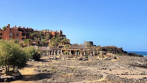Un resort en la playa con varias edificaciones, palmeras y zonas de estar al aire libre.
