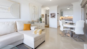 Una sala moderna con un sofá blanco, una mesa de comedor y una cocina al fondo.