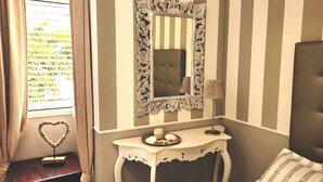 Une pièce avec un mur à rayures, un grand miroir doté d’un cadre orné, une table de chevet agrémentée d’objets décoratifs et une fenêtre avec des rideaux.
