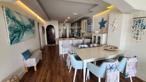 Une cuisine moderne avec des meubles blancs, un îlot central et un coin repas comprenant une table blanche et des chaises bleues.