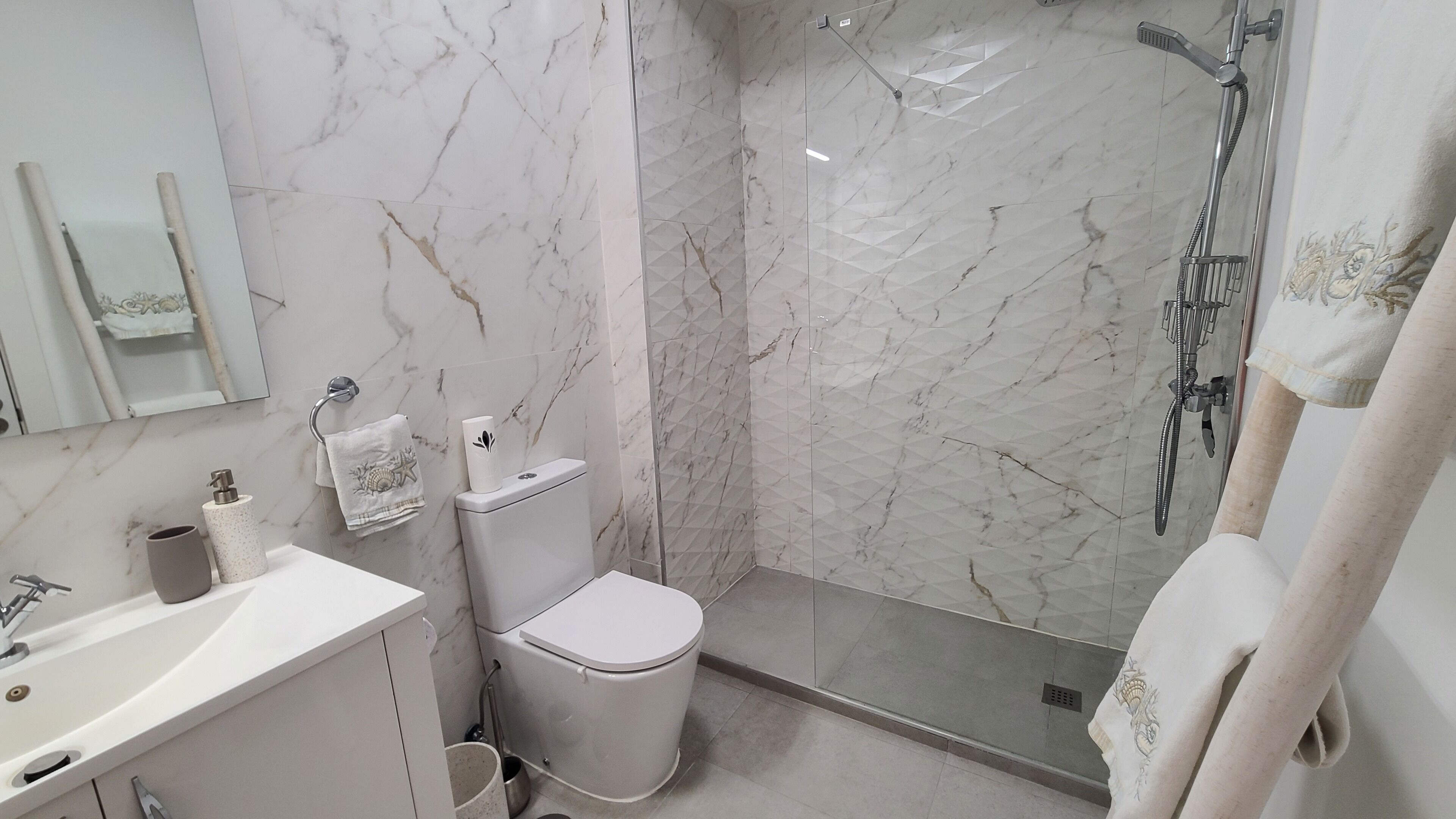 A bathroom with a marble wall, a toilet, a sink, and a glass-enclosed shower.