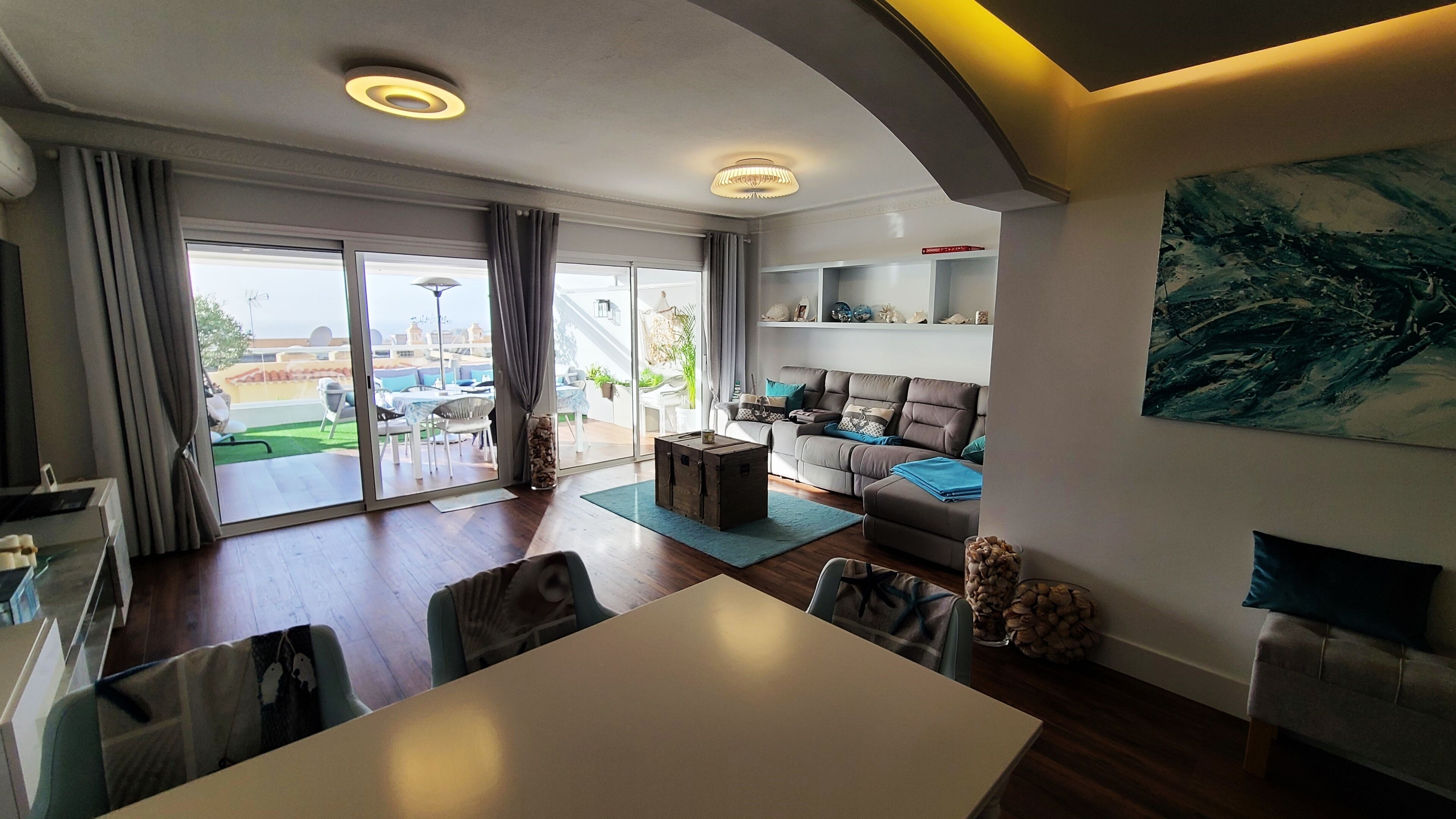 A modern living room with a dining area, large sliding glass doors leading to an outdoor patio, and a view of the cityscape.