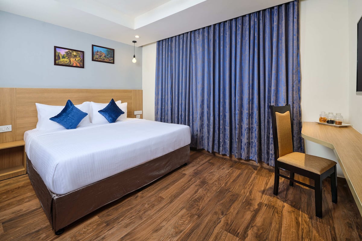Habitación de hotel con una cama grande, un escritorio y una silla. Hay dos cuadros en la pared y una ventana con cortinas azules.