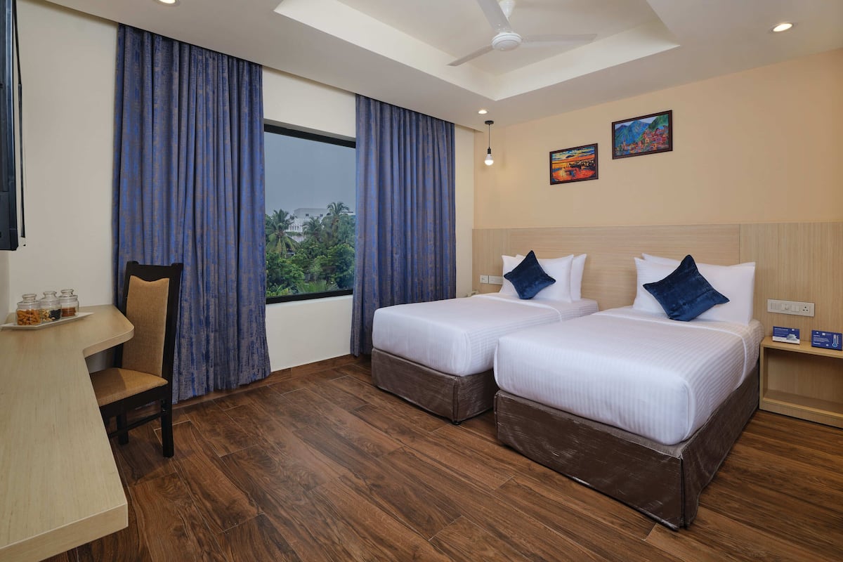 Habitación de hotel con dos camas, un escritorio, una silla y vistas al exterior.