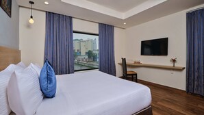 A hotel room with a large bed, a desk, a TV, and a window with curtains. - Essentia Premier Hotel Chennai OMR (Chennai)