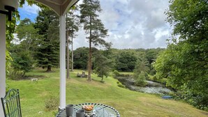 A covered patio with a table and chairs, overlooking a lush garden and a pond. - Deer Leap House (Dorchester)