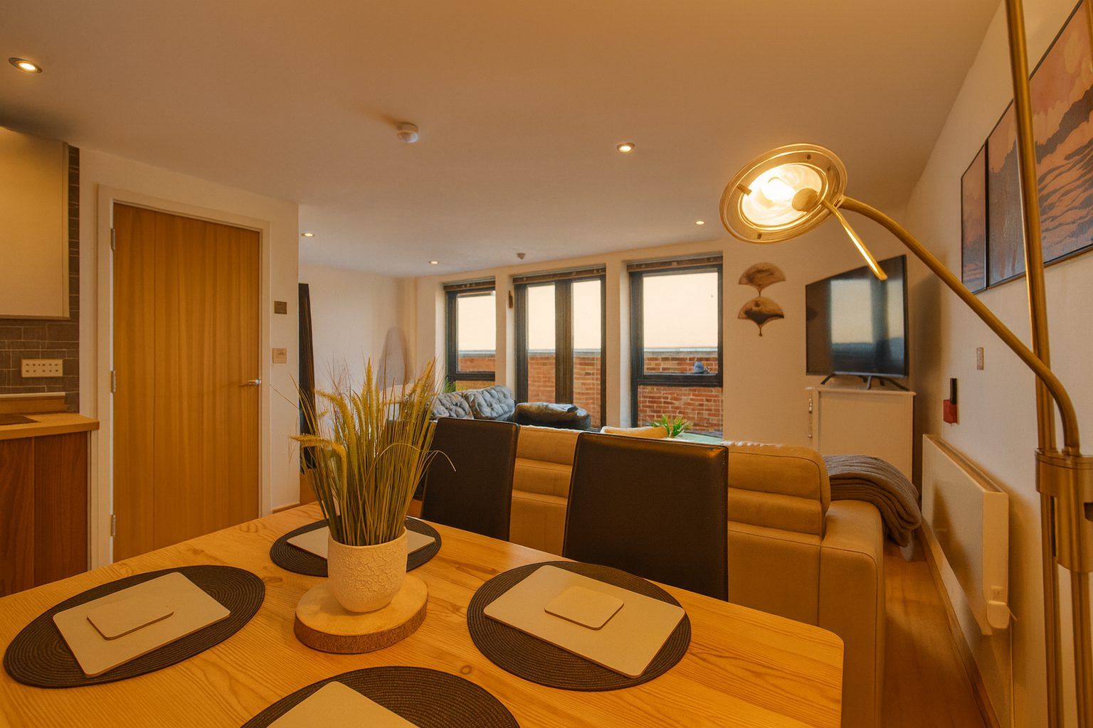 A dining area with a wooden table, chairs, a vase of plants, and a modern floor lamp.
