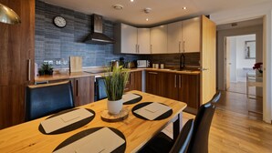 Une cuisine moderne avec des meubles en bois, un mur de fond en briques et un coin repas comprenant une table et des chaises en bois.