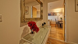 Une pièce avec une table à plateau de verre, une plante en pot rouge, un grand miroir décoratif et un plancher en bois.