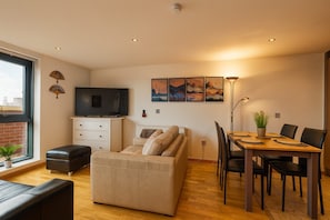 Ein modernes Wohnzimmer mit einer Couch, einem Esstisch mit Stühlen, einem Fernseher und Kunstwerken an der Wand.