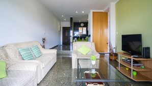 A living room with two sofas, a coffee table, a TV, and a kitchen in the background.