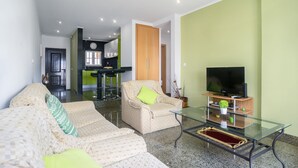 A living room with a sofa, armchair, and glass coffee table. A television is on a wooden stand.