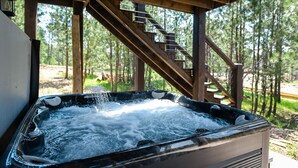 Un bain à remous installé sous une terrasse en bois, avec un escalier menant à une zone boisée.