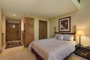 A bedroom with a bed, a nightstand, a lamp, a painting, and wooden doors. - The Evergreen | AC, Pool, Hot Tub, Golf & Ski (Durango)