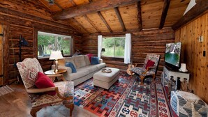 Ein rustikales Blockhaus-Interieur mit einer Couch, Sesseln, einem Fernseher und einem gemusterten Teppich.