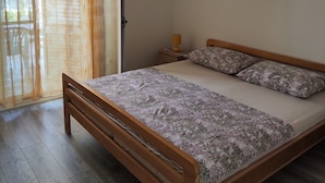 A bedroom with a wooden bed, a nightstand, a lamp, and a sliding glass door with curtains.