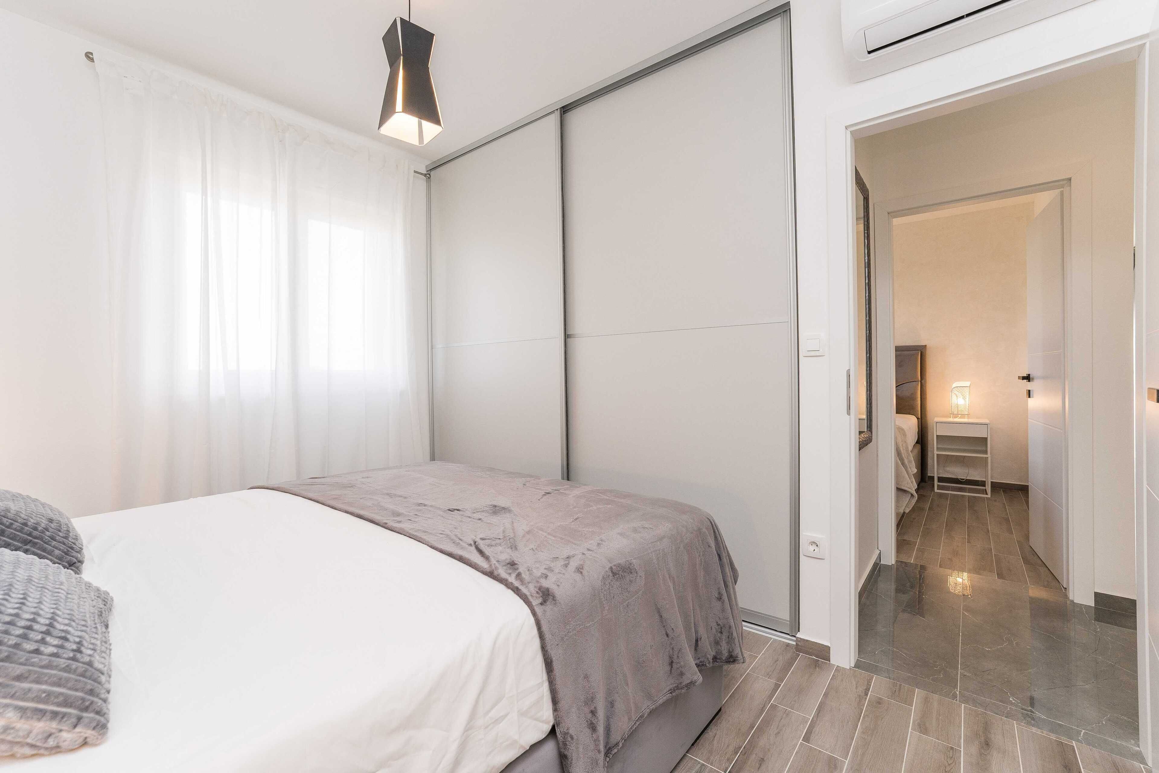 A bedroom with a bed, a bedside table, and a nightstand. There is a door leading to another room.