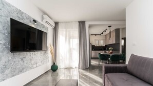 Una sala de estar moderna con televisor de pantalla plana, un sofá gris, una mesa de centro y una zona de comedor con sillas verdes.