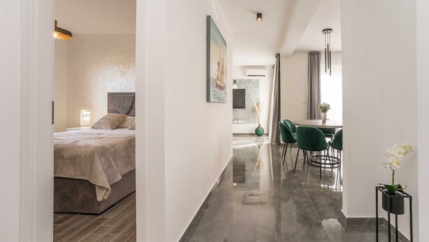 Una habitación de hotel moderna con una cama, una zona de comedor con sillas y un pasillo que conduce a otra habitación.