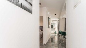 Un pasillo moderno con piso pulido, una zona de comedor con sillas verdes y un espacio de sala con sofá.