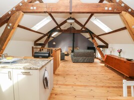 Una habitación estilo loft con techo inclinado, vigas de madera, una zona de cocina con pileta y escurreplatos, un sofá y un televisor.
