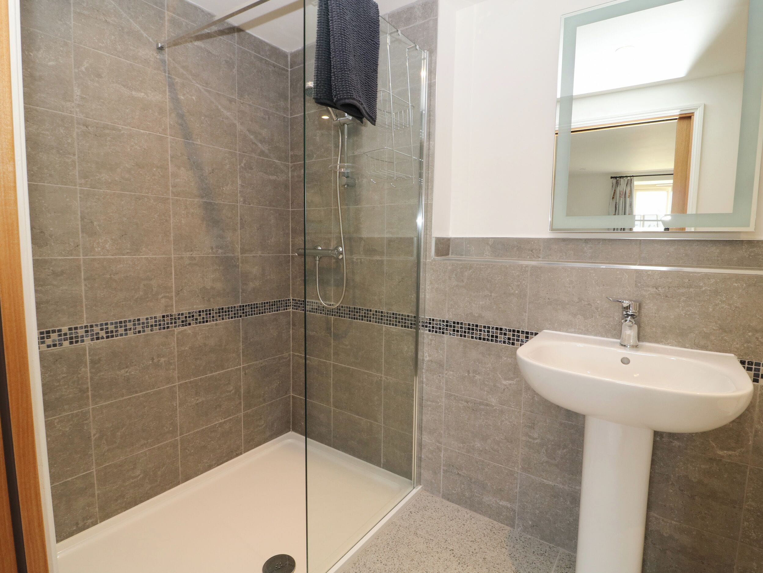 A modern bathroom with a glass shower enclosure, a white sink, and a tiled shower area.