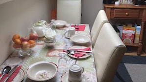 Una mesa de comedor dispuesta con platos, tazones y una tetera, con una lámpara y una caja de cereal al fondo.