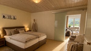 A bedroom with a bed, a nightstand, a lamp, a robe, a chair, and a view of the outdoors.