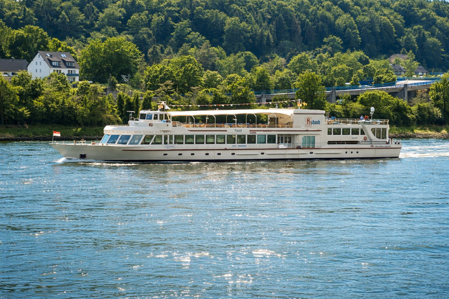 A riverboat with a flat deck, multiple windows, and a flag.
