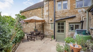 A stone building with a green door, a patio with a table and umbrella, and potted plants. - Traditional Cotswold stone cottage sleeps 7 guests in 3 bedrooms - Little Mullions (Little Rissington, near Bourton-on-the-Water)