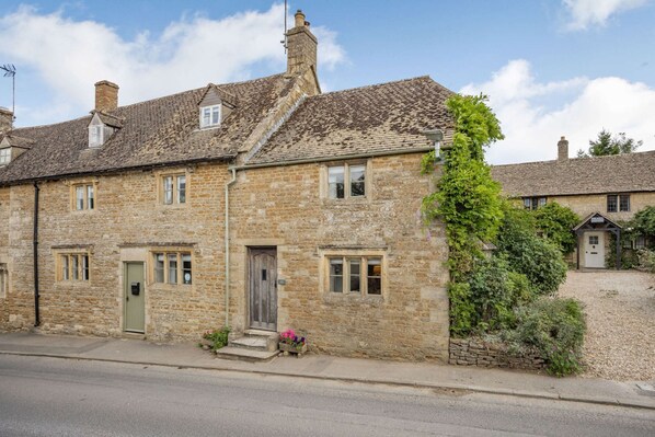 A stone building with a traditional design, featuring a small window and a door, and a garden area with plants and flowers.
