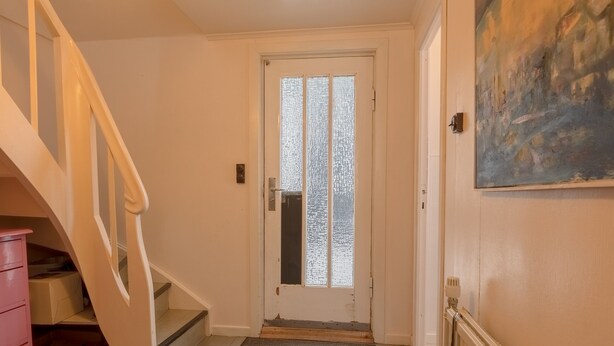 Un pasillo con una escalera, una puerta con paneles de vidrio esmerilado, un radiador y un cuadro en la pared.