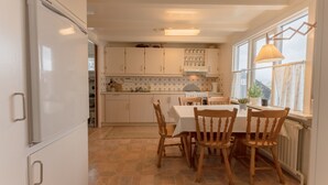 Una cocina con una mesa de comedor y sillas, un refrigerador, armarios y un ventanal con cortinas.