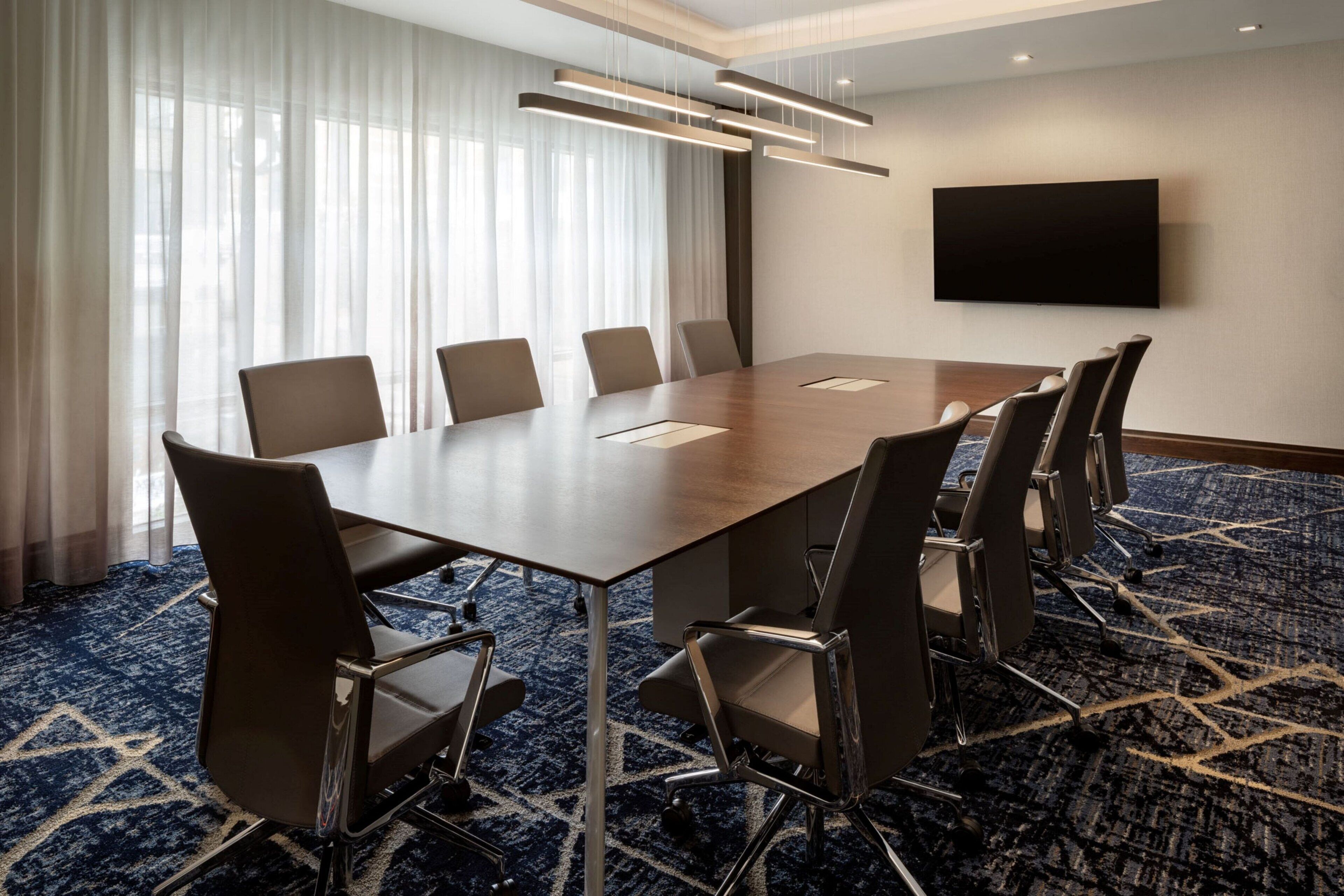Une salle de conférence équipée d’une grande table, de six chaises, d’un téléviseur à écran plat et d’une moquette à motifs.