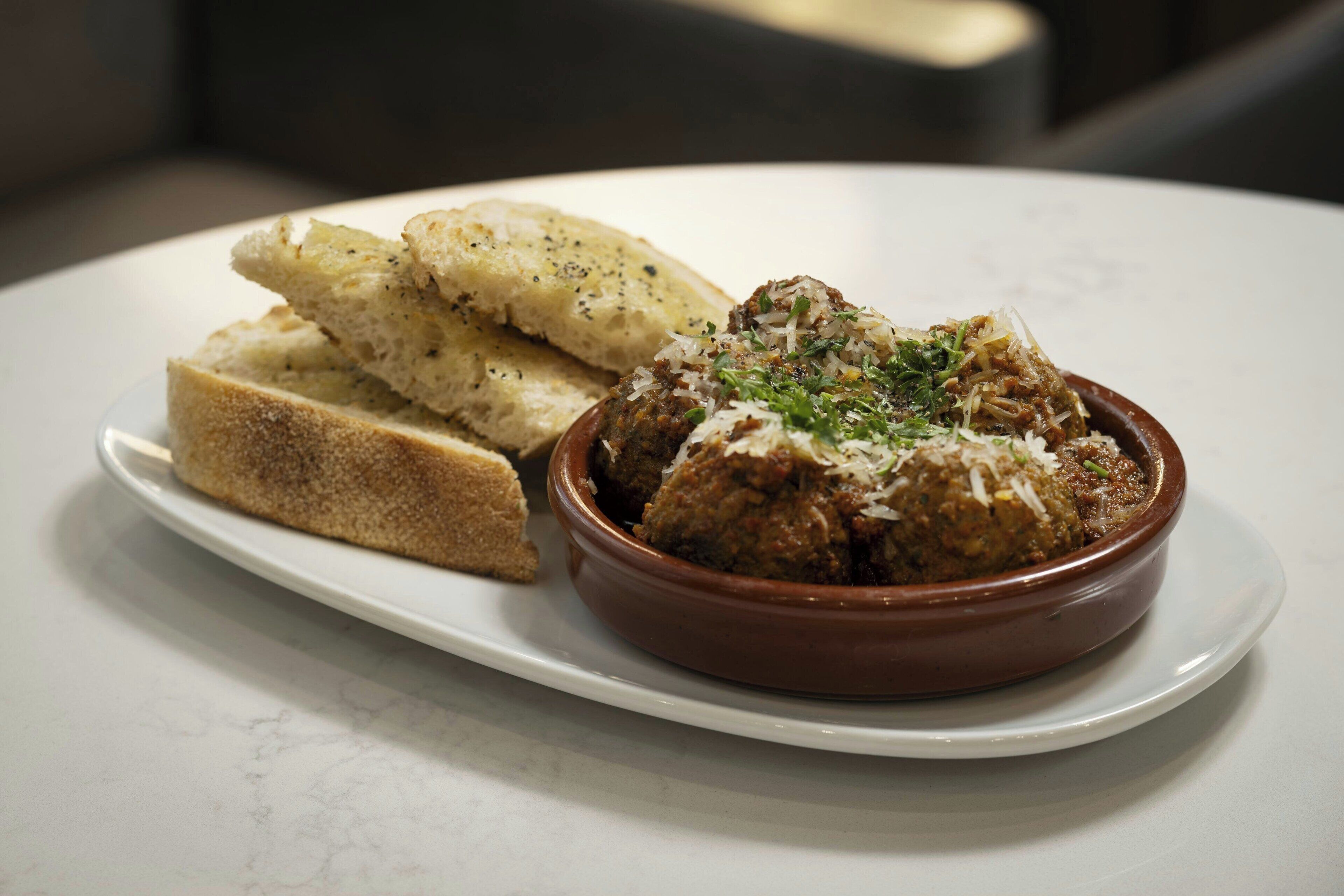 A plate with meatballs and grated cheese, accompanied by slices of bread.
