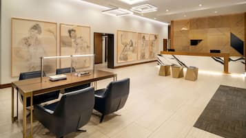 A modern hotel lobby with a wooden reception desk, black leather chairs, and framed artwork on the walls.