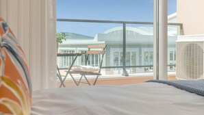 A balcony with a view of a building with a curved roof, a folding chair, and a large window. - Casa Makin at Boa Vista Golf Resort, Bayview Village (Lagos)